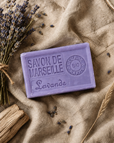 Savon de Marseille lavande sur un lin sable, avec un petit bouquet de lavande séchée, du bois clair et des brins d’herbe