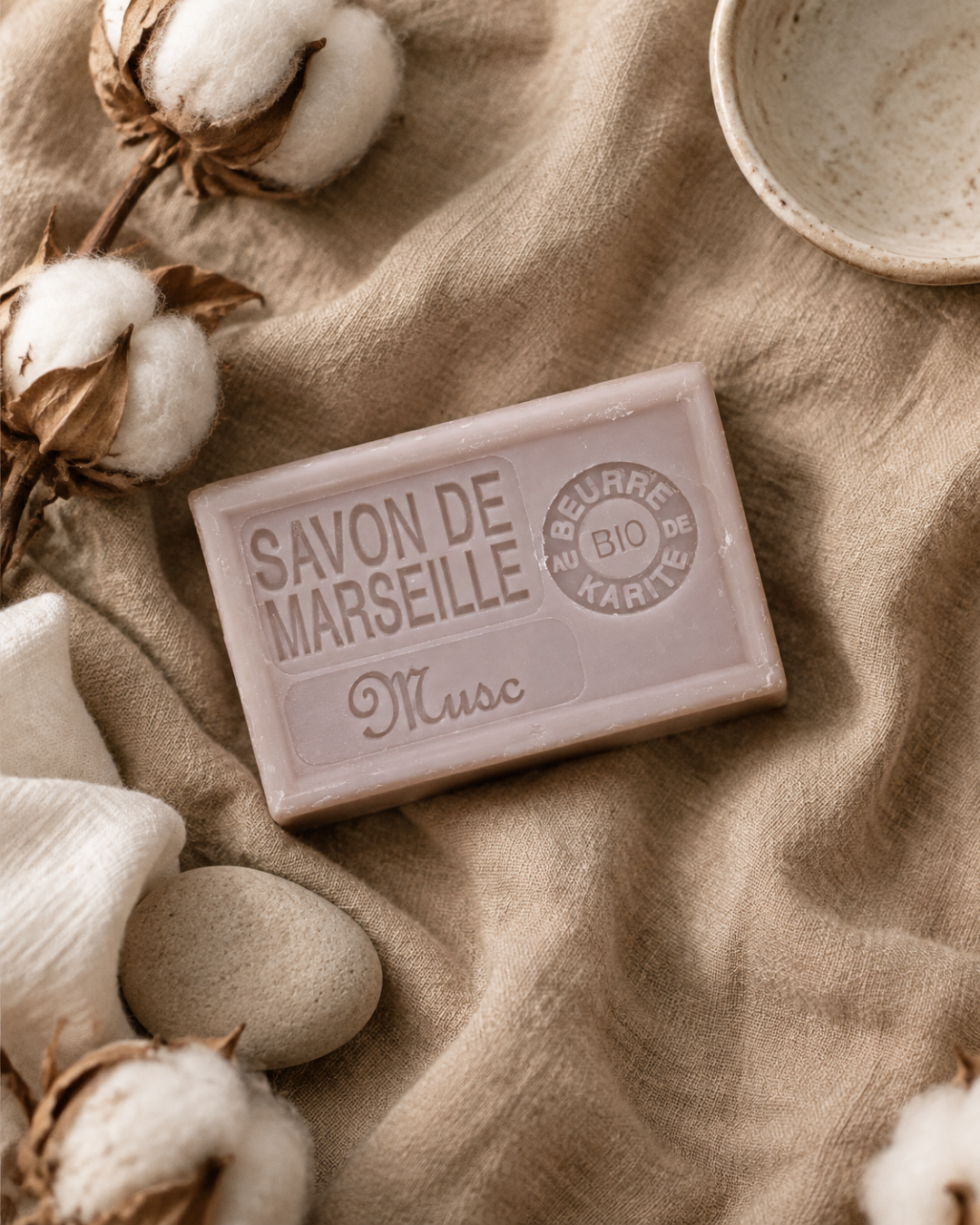 Savon de Marseille musc sur un lin beige, entouré de capsules de coton et de galets lisses
