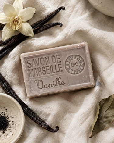 Savon de Marseille vanille sur un lin crème, avec des gousses de vanille, une orchidée claire et un petit bol en céramique