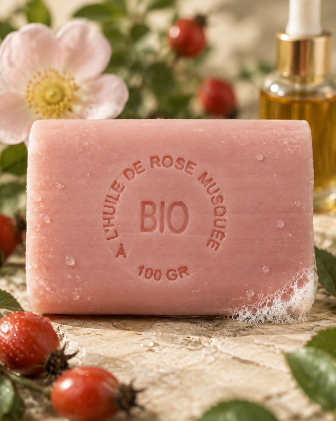 Gros plan sur le tampon gravé d’un savon à l’huile de rose musquée, avec gouttelettes et cynorrhodons flous